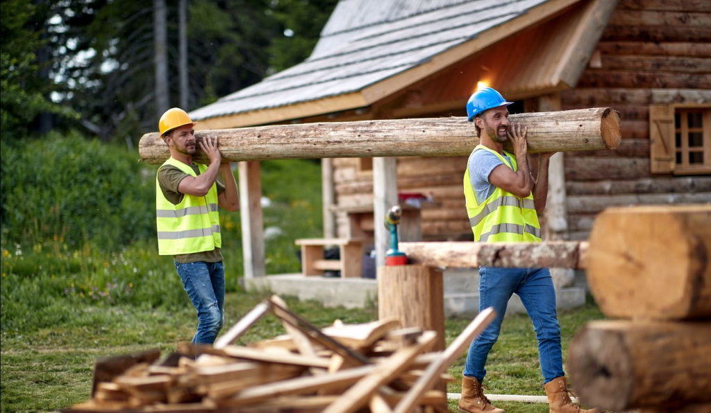 Zwei Arbeiter tragen einen Baumstamm gemeinsam.